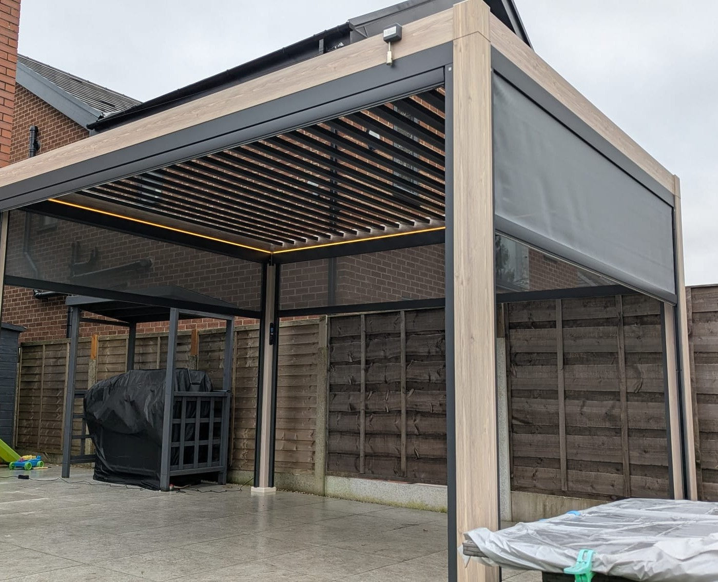 LuxShade™ 3×3m Aluminium Pergola – LEDs, Double-Layer Louvres & 3 Windscreens - Oak Effect